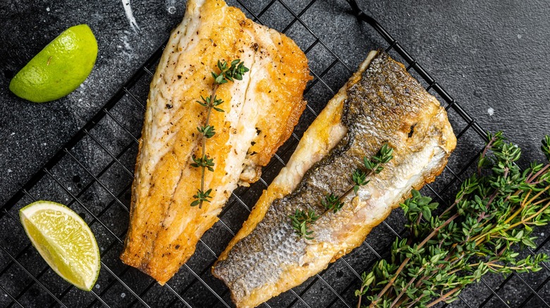 Two cooked fish filets with the skin on resting on a baking sheet with lime and rosemary