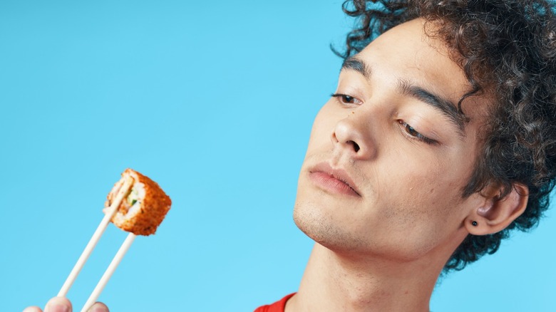 Man holding sushi roll with chopsticks, looking unsure