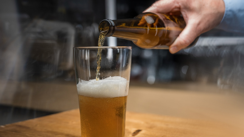 hand pours bottle of beer into glass