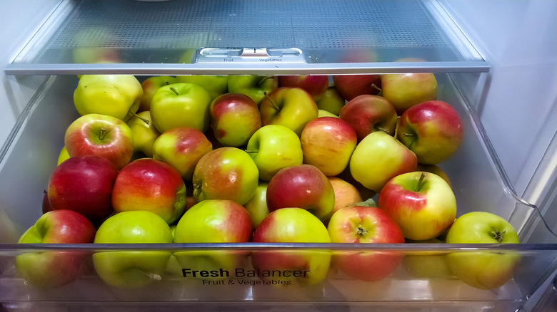 Green and red apples in an open refrigerator drawer.