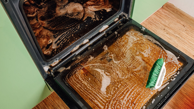 An open oven being cleaned with a green and white hand brush