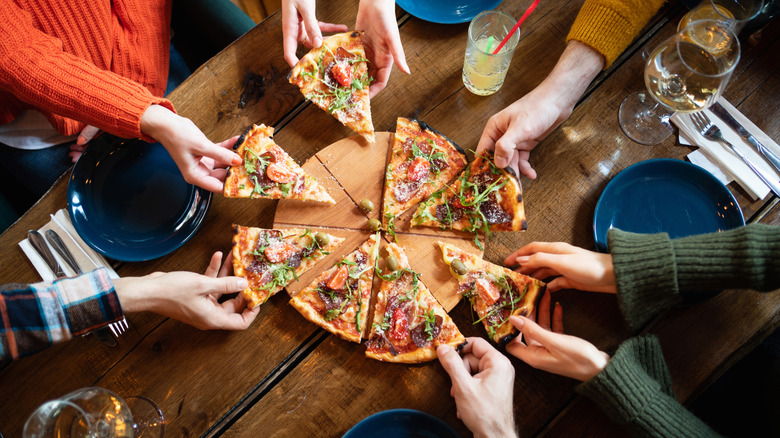 Group of people eating pizza slices together at a table