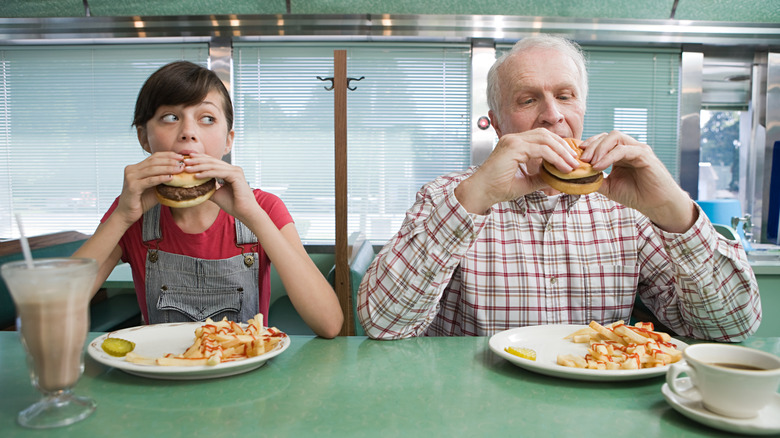 Younger woman sitting with older man eating burgers at a diner