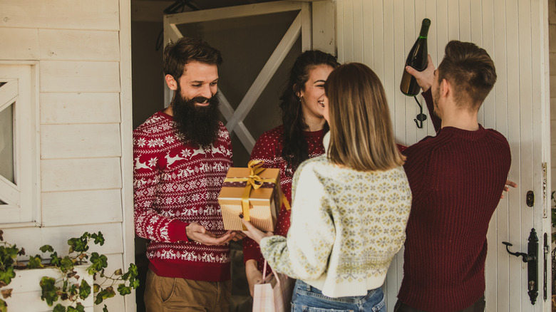 Couples greet each other at door with gifts.