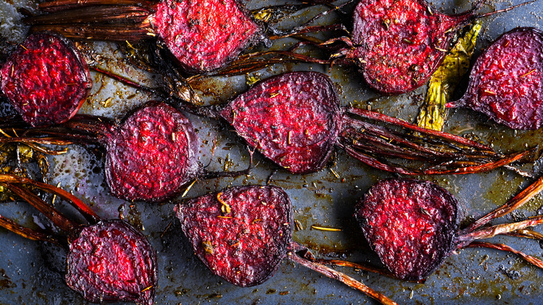 Multiple roasted beets sliced in half on a baking tray