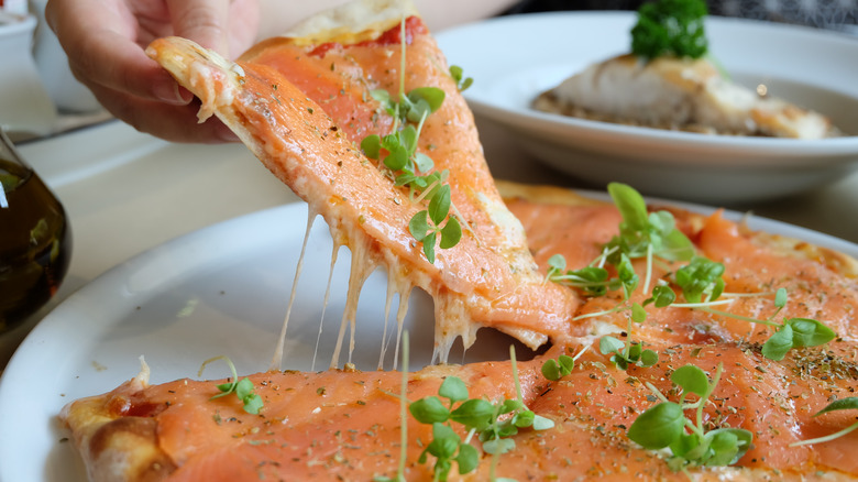 A diner picking up a slice of pizza topped with smoked salmon