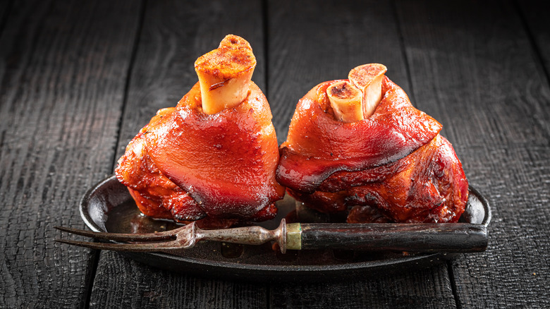 Cooked smoked ham hocks with spices on a small plate with a fork