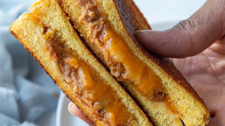 hand holding a halved pulled pork grilled cheese