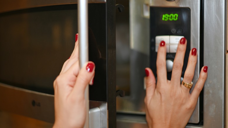 A woman clicking a button on a microwave while closing its door.