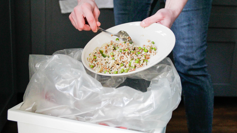 A person scraping food into the trash