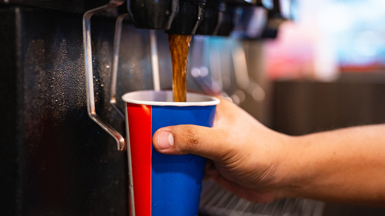 A person's hand holds a soda cup under a running dispenser