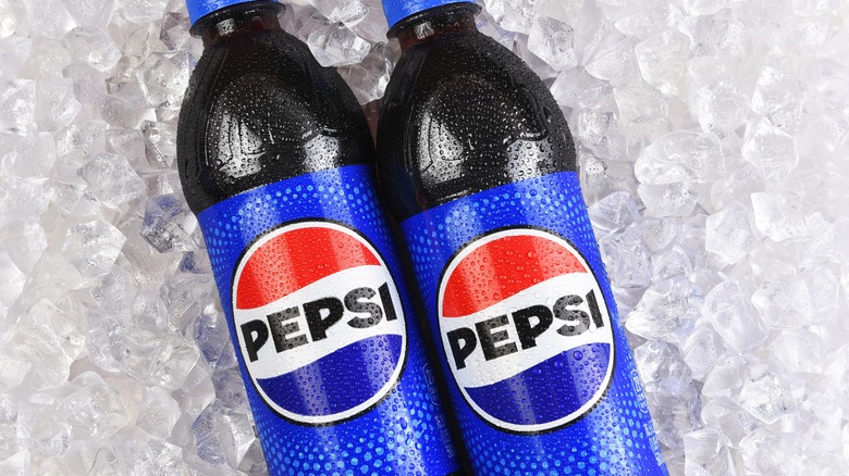 Two Pepsi bottles laying on ice cubes