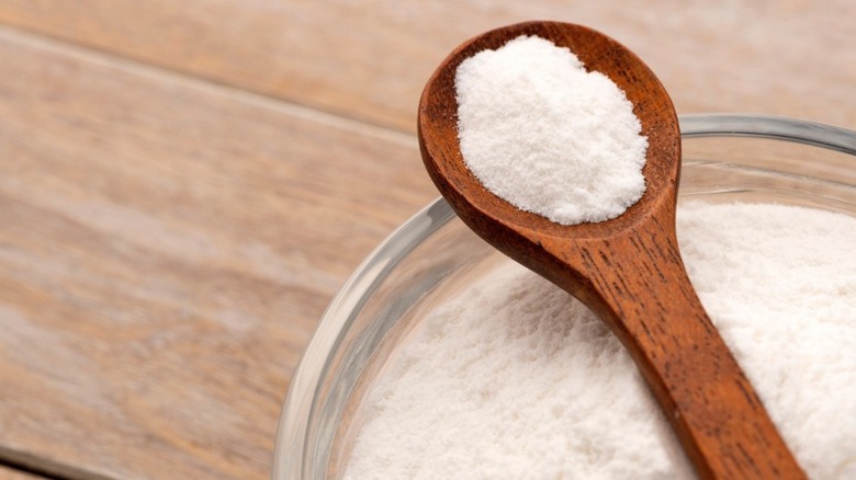 A wooden spoon holding baking soda above glass dish of baking soda