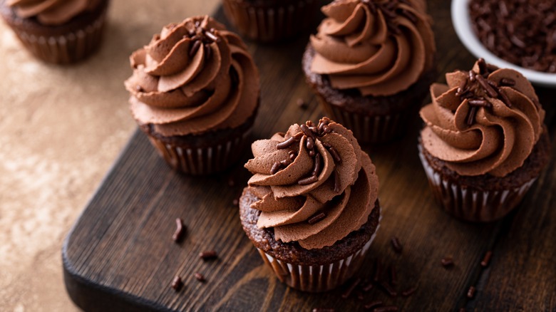 Chocolate cupcakes with chocolate frosting and sprinkles on a wooden board