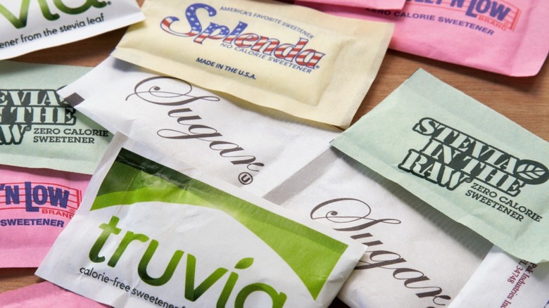 Scattered sweetener packets including sugar, brands of stevia, and splenda