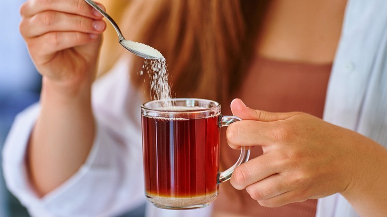 spoon of sweetener being added to cup of tea