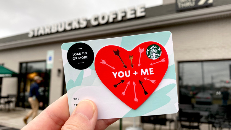 Customer holds a Valentine's Day-themed gift card before Starbucks storefront