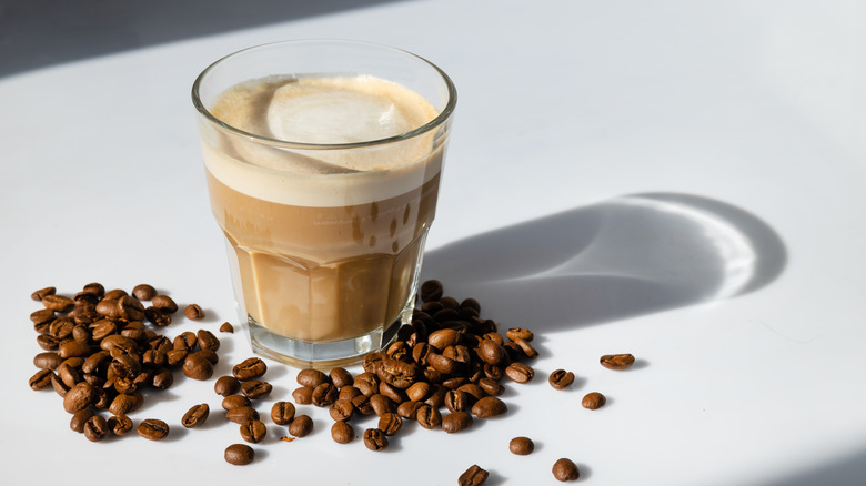 cortado espresso in glass with beans on table