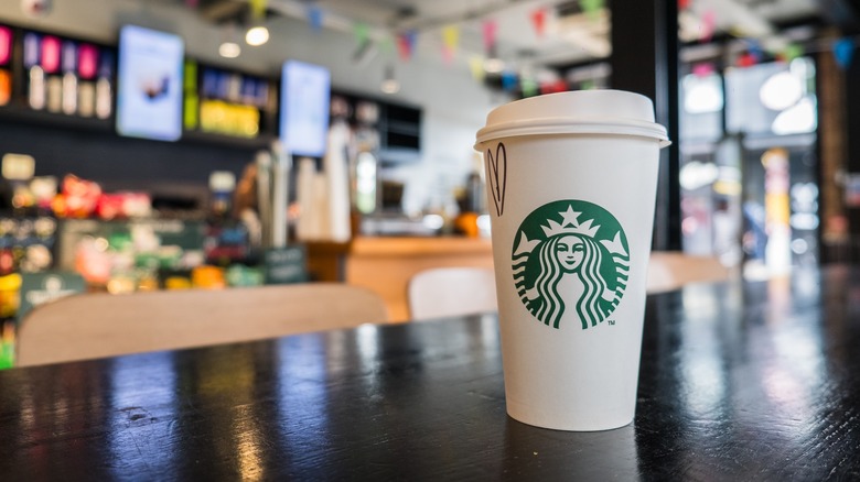 To go Starbucks cup sitting on a table with a Starbucks store in the background