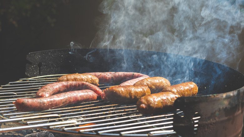 Hot dogs and sausages producing smoke while cooking on the grill