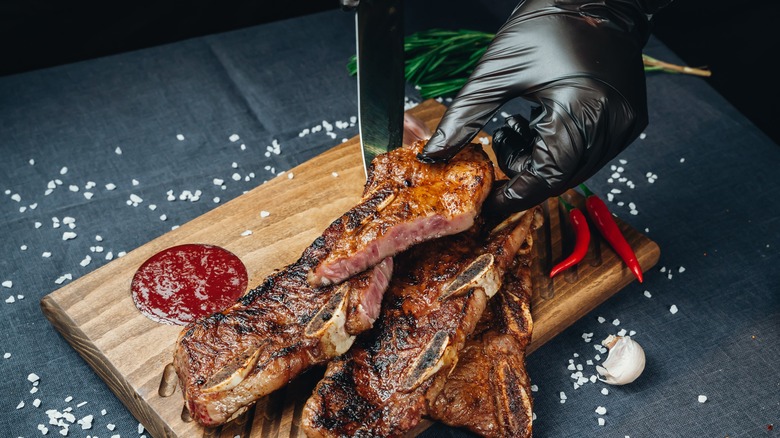 gloved hands cutting steak on board