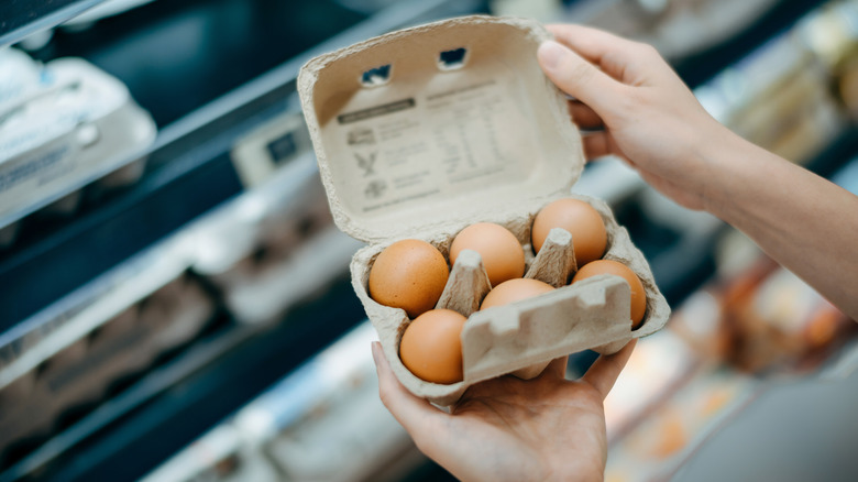 Hands hold an open carton of eggs at the grocery store.