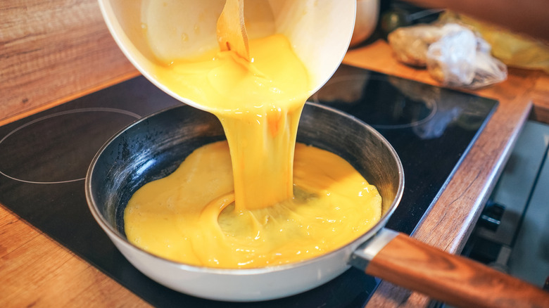 Raw eggs that have been whisked together are poured into a pan on a stove.