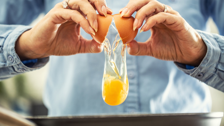 Two hands are shown cracking an egg into a pan.