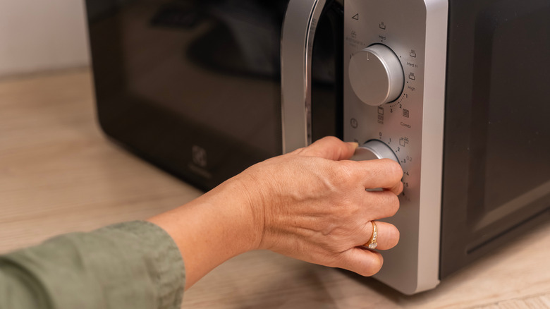 A hand adjusts a microwave setting.