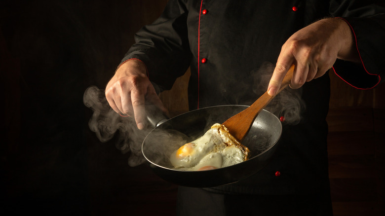 A chef flips a fried egg in a skillet.