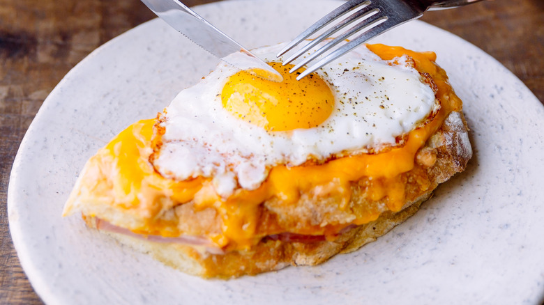 A knife and fork are used to cut into a fried egg.