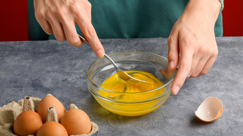 Two hands are shown beating egg with a fork.