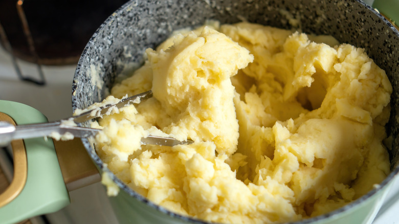 Freshly mashed potatoes in a grey bowl with a light green handle