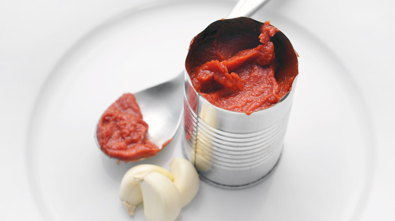 Open can of tomato paste with garlic cloves and spoon