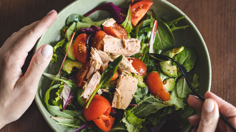 Hands holding bowl of salad topped with tuna