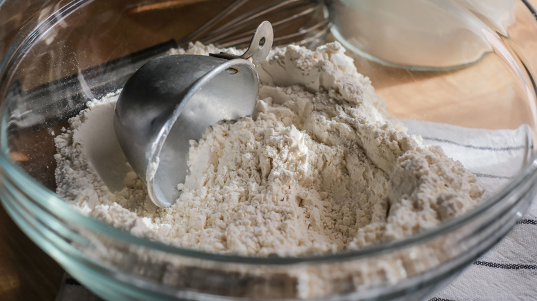 flour in clear bowl with a metal measuring cup