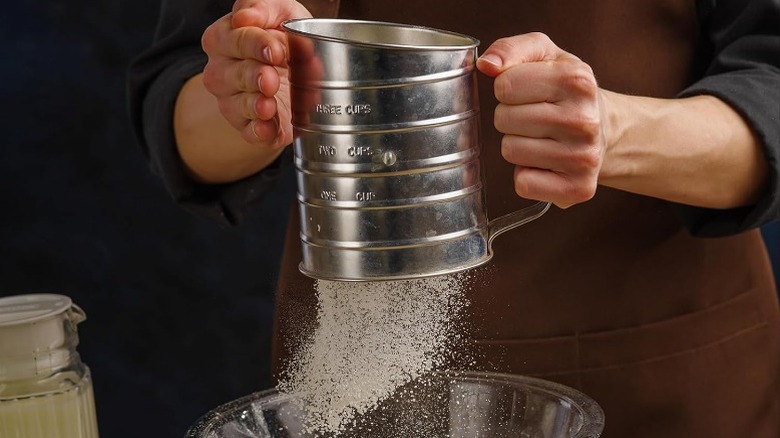 hands holding a flour sifter over a bowl