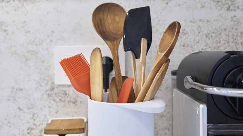 A white pot filled with wooden spoons and other kitchen utensils