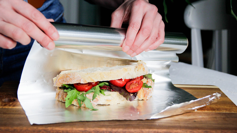 A person wrapping a salad sandwich in aluminum foil