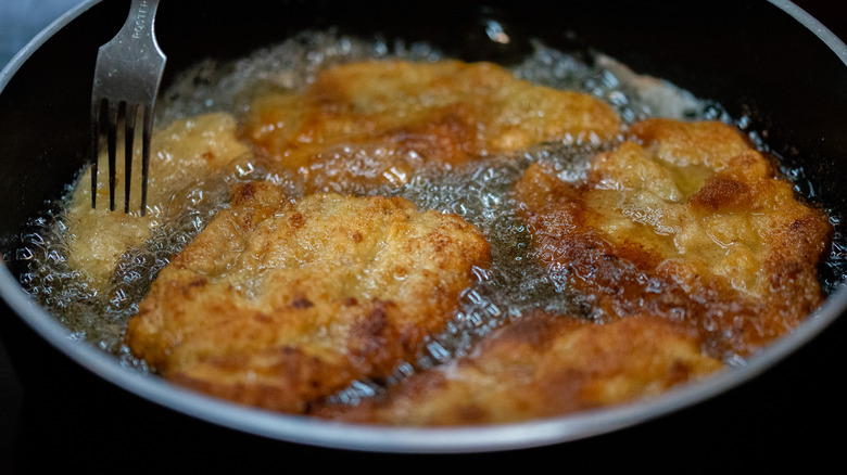 Chicken frying in oil inside a black pan