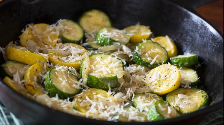 Cast iron pan filled with round slices of yellow squash and zucchini with grated parmesan on them