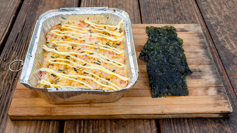 An aluminum tray of sushi bake on a wooden board served with dried seaweed sheets