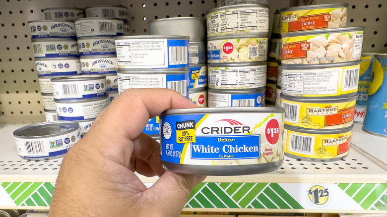 A hand holding a can of chicken in a grocery store