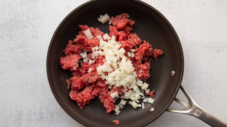 raw ground beef and diced onion in skillet