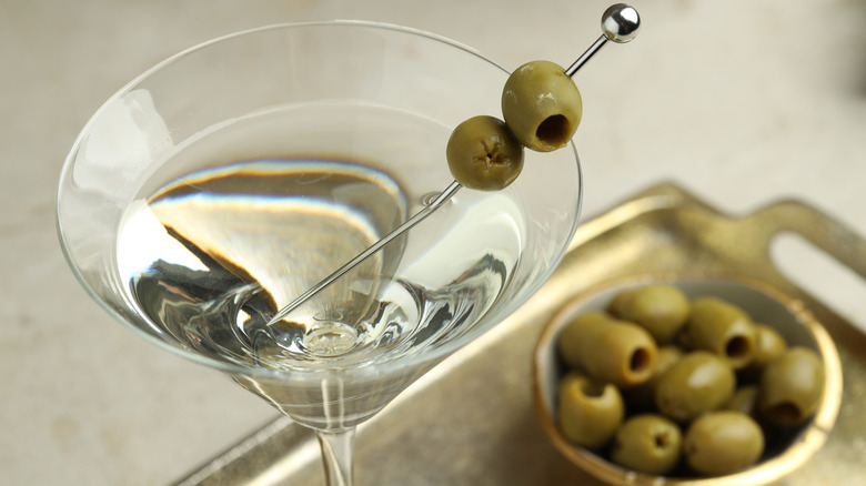 Glass of dry martini with bowl of olives in background