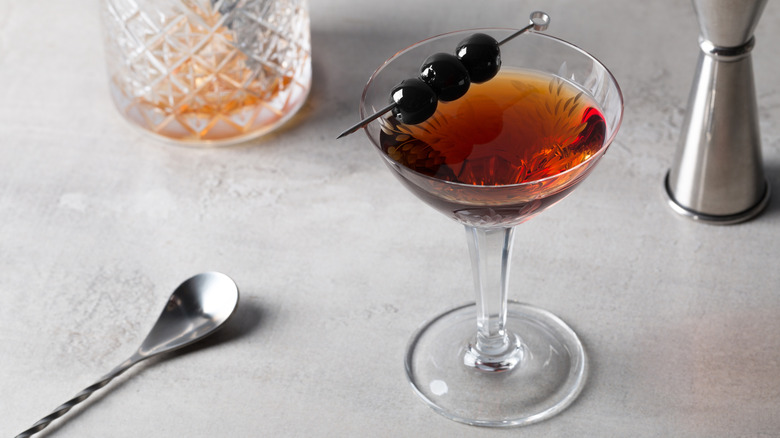 Manhattan cocktail garnished with cherries with a stirring spoon