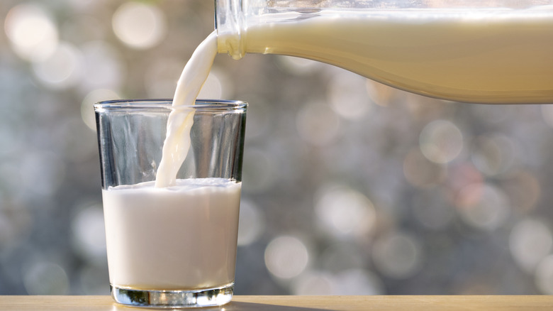 milk being poured from a glass bottle into a glass on a wooden table