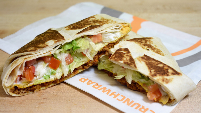 Two halves of a Crunchwrap Supreme lay on a paper wrapper