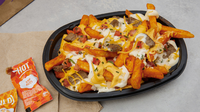 An order of Taco Bell Steak Garlic Nacho Fries sits in a bowl next to hot sauce