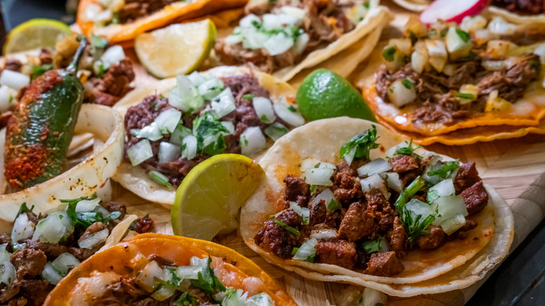 a table full of tacos with lime wedges and peppers